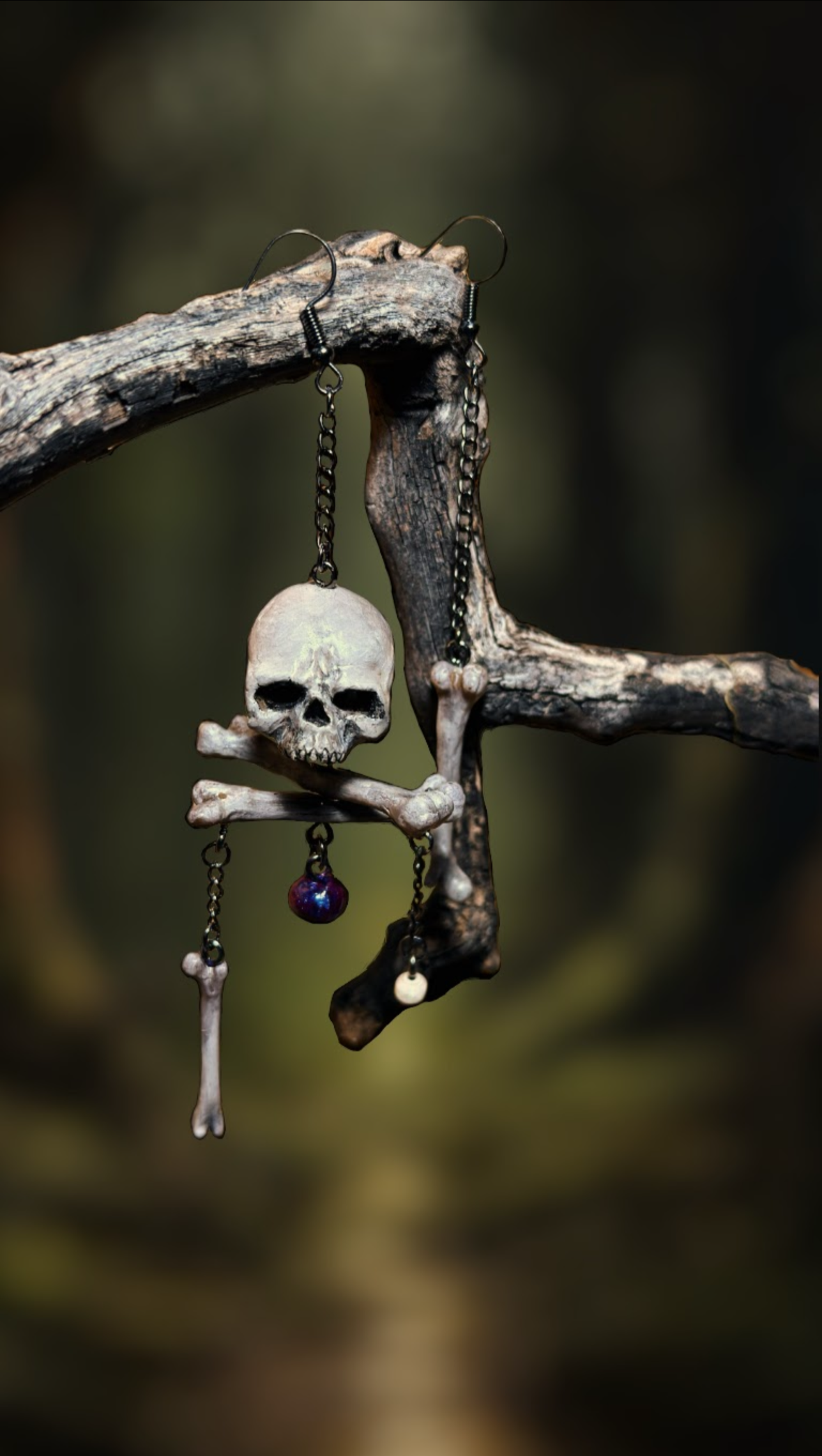 Skull and bone earring with a purple gemstone hanging from a branch